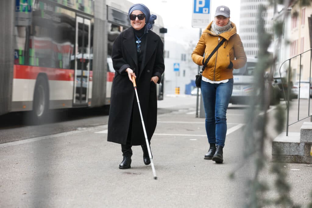 Eine stark sehbeeinträchtigte Frau übt den Umgang mit dem weissen Stock mit einer Expertin von der obvita Sehberatung.