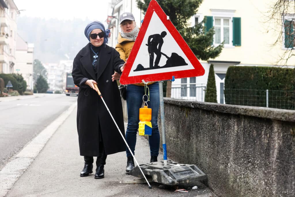 Eine stark sehbeeinträchtigte Frau übt den Umgang mit dem weissen Stock mit einer Expertin von der obvita Sehberatung.