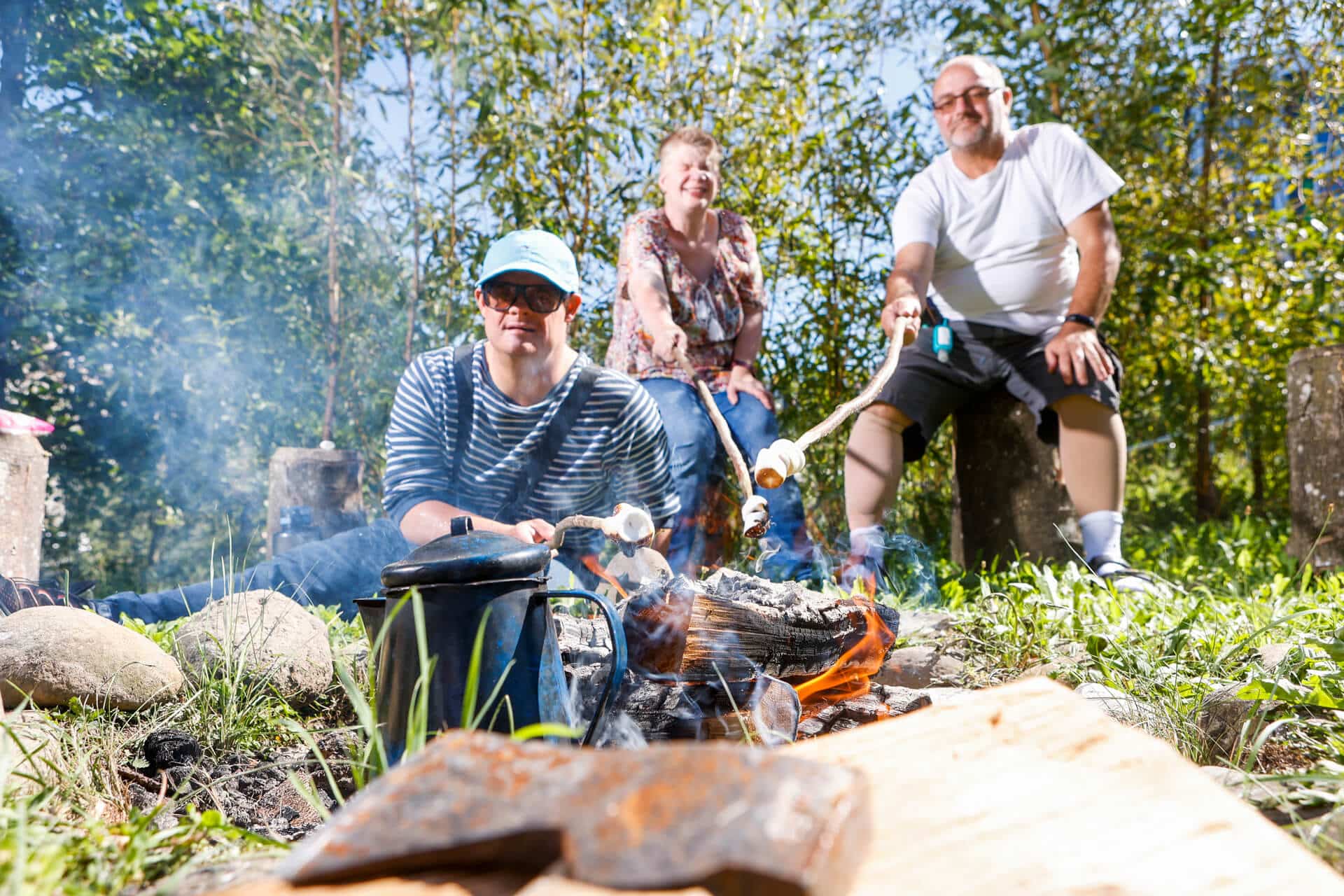 Eine Gruppe von Menschen in der obvita Talentwerkstatt grillt Marshmallows über einem Lagerfeuer in der Natur. Sie geniessen gemeinsam die entspannte Atmosphäre und das Erlebnis im Freien.