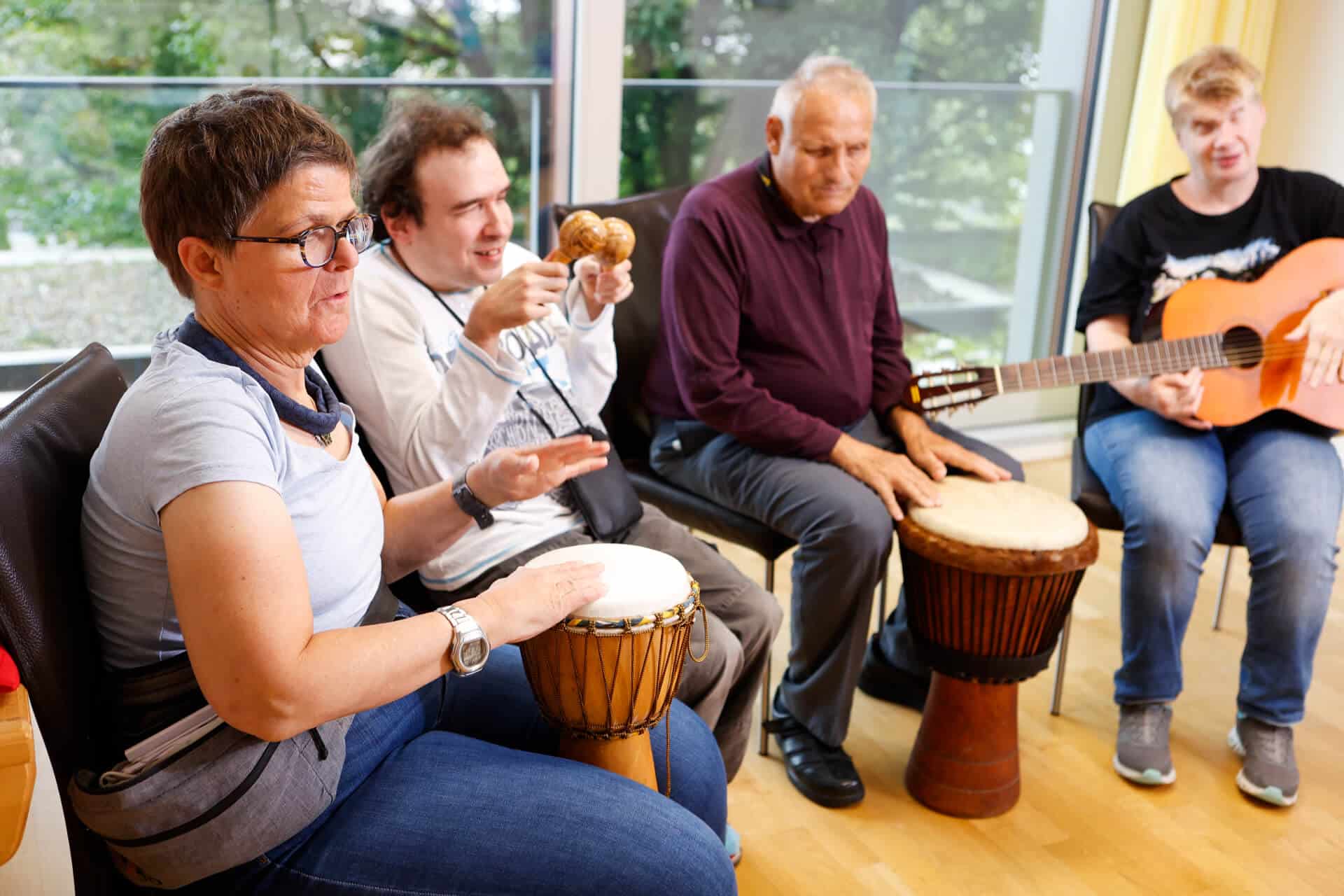 Eine Gruppe von Menschen in der obvita Talentwerkstatt musiziert gemeinsam. Sie spielen verschiedene Instrumente wie Trommeln, Maracas und Gitarre und geniessen den Moment der Gemeinschaft und Kreativität.