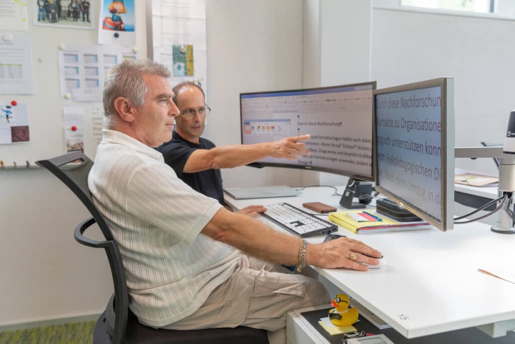 Ein Experte der Sozialinformatik erklärt einem Sehbeeinträchtigten die Bedienung eines Computers.
