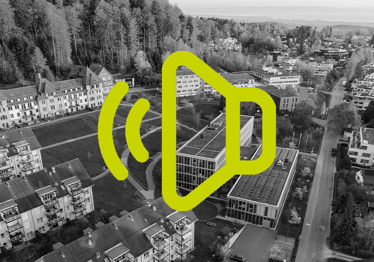 Eine Schwarz-Weiß-Luftaufnahme eines Wohn- und Stadtgebiets mit Häusern und Bäumen, überlagert von einem großen gelben Lautsprechersymbol und Schallwellen in der Mitte.